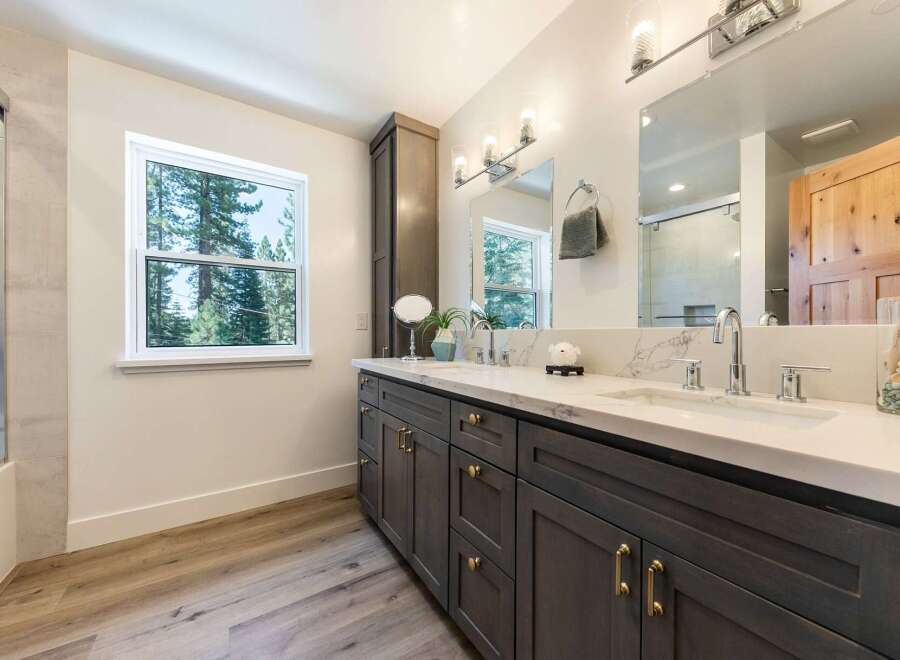 This modern bathroom features a spacious double vanity with a sleek white countertop and dark wood cabinetry, complemented by elegant brass hardware.
