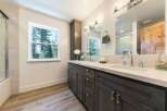This modern bathroom features a spacious double vanity with a sleek white countertop and dark wood cabinetry, complemented by elegant brass hardware.