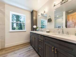 This modern bathroom features a spacious double vanity with a sleek white countertop and dark wood cabinetry, complemented by elegant brass hardware.