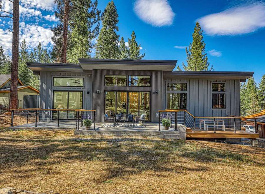 Experience modern mountain living in this stunning contemporary home, featuring sleek vertical siding and expansive windows that invite the natural beauty of the surrounding pine forest indoors.