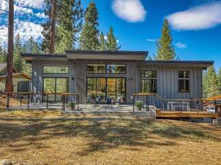 Experience modern mountain living in this stunning contemporary home, featuring sleek vertical siding and expansive windows that invite the natural beauty of the surrounding pine forest indoors.
