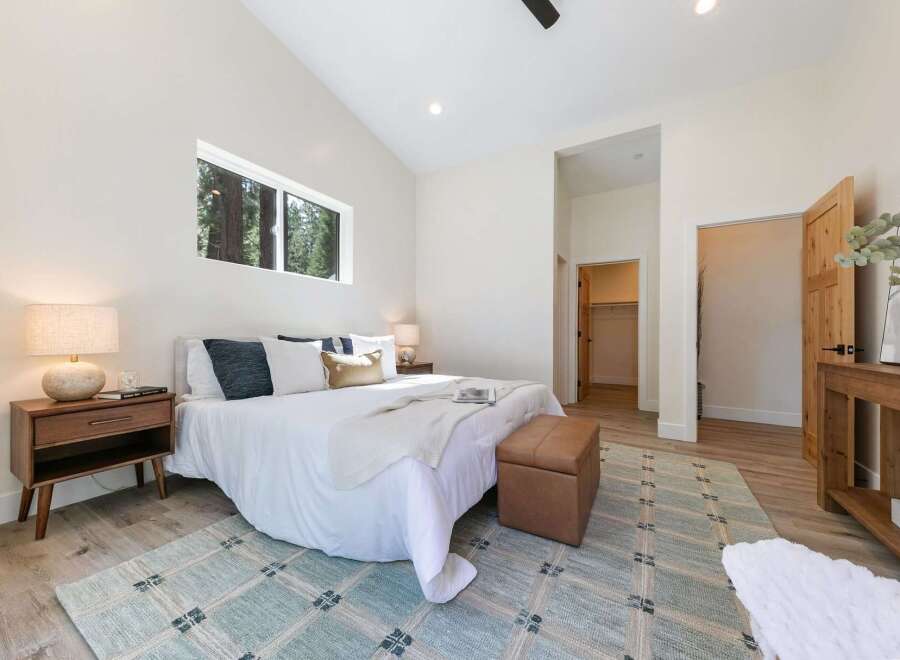 Experience modern comfort in this spacious bedroom, featuring a vaulted ceiling and a large horizontal window offering serene forest views.
