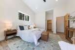 Experience modern comfort in this spacious bedroom, featuring a vaulted ceiling and a large horizontal window offering serene forest views.