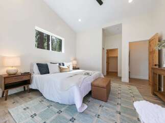 Experience modern comfort in this spacious bedroom, featuring a vaulted ceiling and a large horizontal window offering serene forest views.