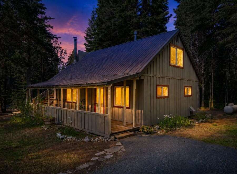 Nestled amongst tall trees, this charming cabin offers a cozy retreat with warm, inviting lights glowing from its windows.