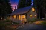 Nestled amongst tall trees, this charming cabin offers a cozy retreat with warm, inviting lights glowing from its windows.