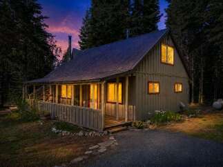 Nestled amongst tall trees, this charming cabin offers a cozy retreat with warm, inviting lights glowing from its windows.