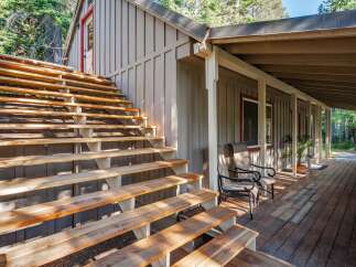 Ascend to this charming cabin retreat via a sturdy wooden staircase, leading to a welcoming covered porch perfect for enjoying the surrounding nature.