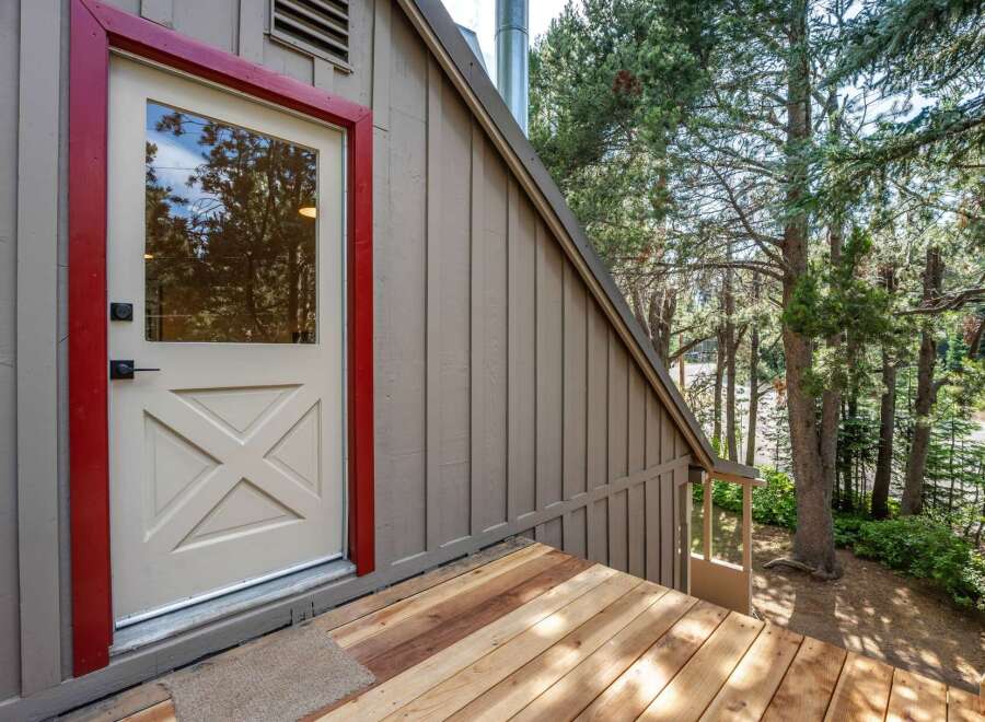 Step onto the charming wooden deck of this mountain retreat, leading to a welcoming door with a striking red frame.