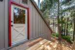 Step onto the charming wooden deck of this mountain retreat, leading to a welcoming door with a striking red frame.