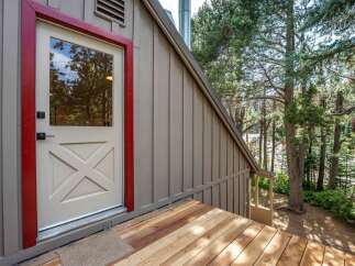 Step onto the charming wooden deck of this mountain retreat, leading to a welcoming door with a striking red frame.