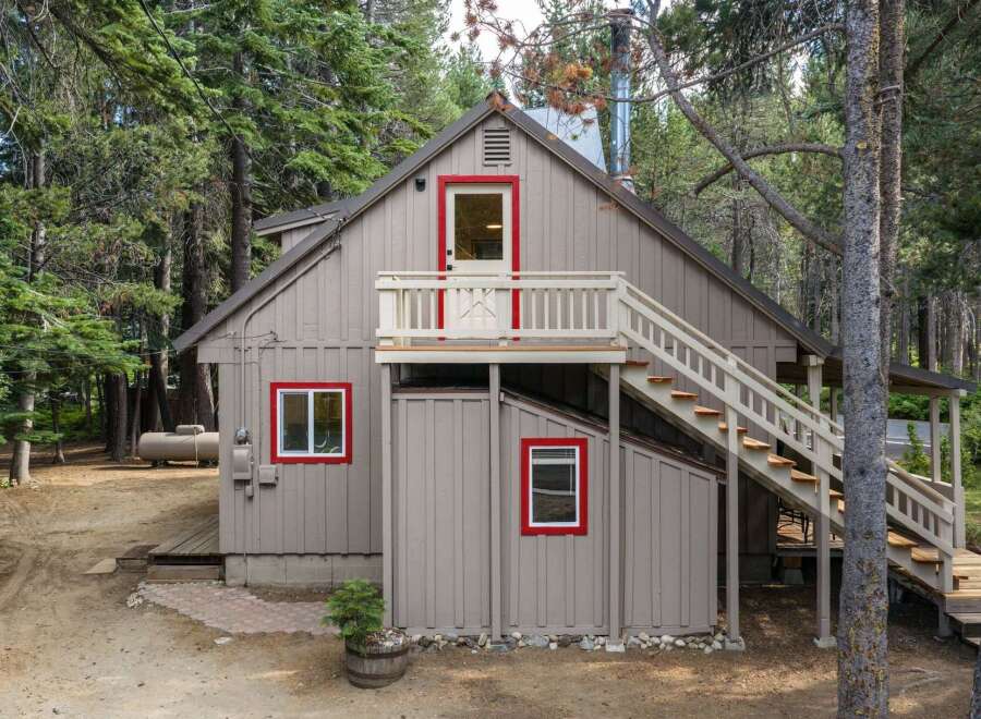Nestled amongst tall pine trees, this charming cabin offers a rustic retreat with its distinctive red-trimmed windows and doors.