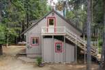 Nestled amongst tall pine trees, this charming cabin offers a rustic retreat with its distinctive red-trimmed windows and doors.