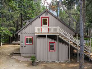 Nestled amongst tall pine trees, this charming cabin offers a rustic retreat with its distinctive red-trimmed windows and doors.