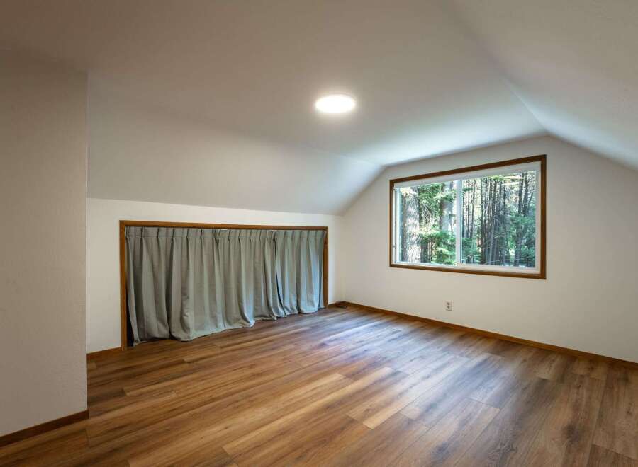 Discover this charming attic room, featuring a large window that floods the space with natural light and offers serene forest views.