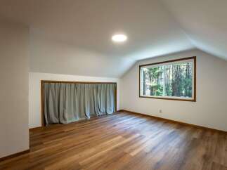 Discover this charming attic room, featuring a large window that floods the space with natural light and offers serene forest views.