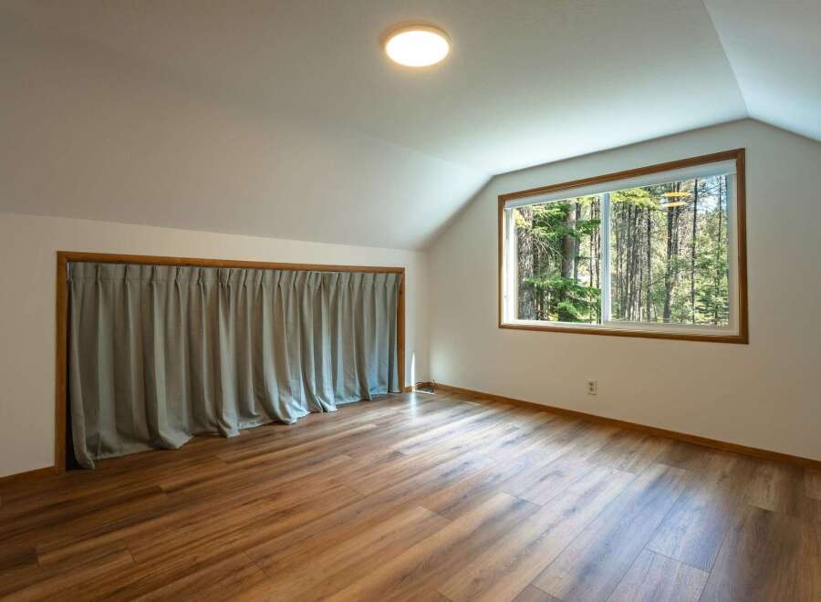This attic room features a large window with a view of the surrounding forest, bringing natural light into the space.