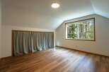 This attic room features a large window with a view of the surrounding forest, bringing natural light into the space.