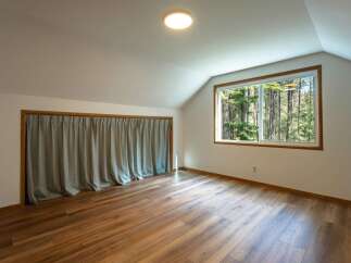 This attic room features a large window with a view of the surrounding forest, bringing natural light into the space.