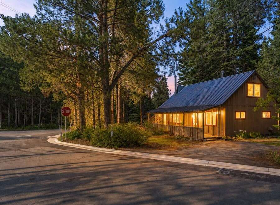 Nestled amongst tall pine trees, this charming cabin offers a cozy retreat with its warm, inviting interior lights glowing through the windows.