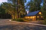 Nestled amongst tall pine trees, this charming cabin offers a cozy retreat with its warm, inviting interior lights glowing through the windows.
