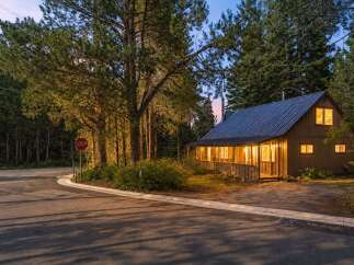 Nestled amongst tall pine trees, this charming cabin offers a cozy retreat with its warm, inviting interior lights glowing through the windows.