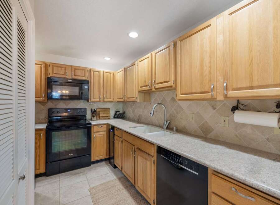 This charming kitchen features light wood cabinetry and a sleek black range with a matching microwave above.