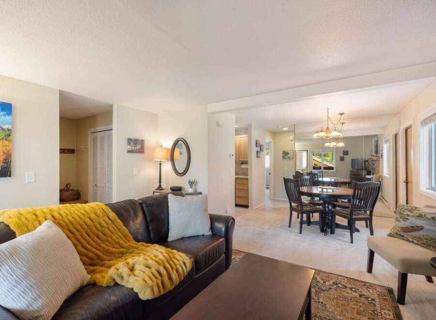 Experience comfortable living in this inviting open-concept space, featuring a spacious living area with a plush leather sofa and a cozy yellow throw, perfect for relaxation.