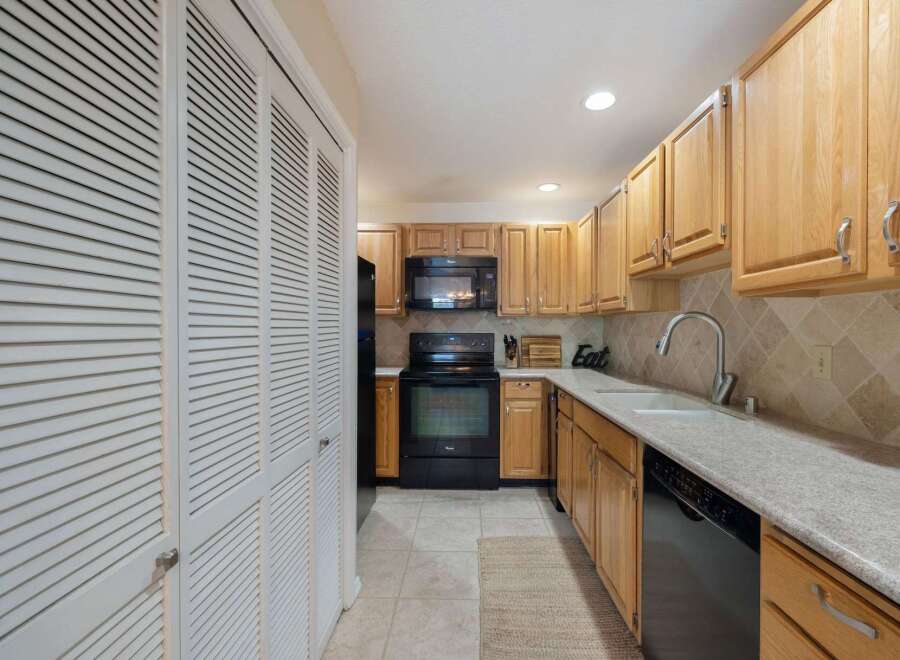 Discover this charming kitchen featuring light wood cabinetry and a sleek black appliance suite, including a microwave and oven.