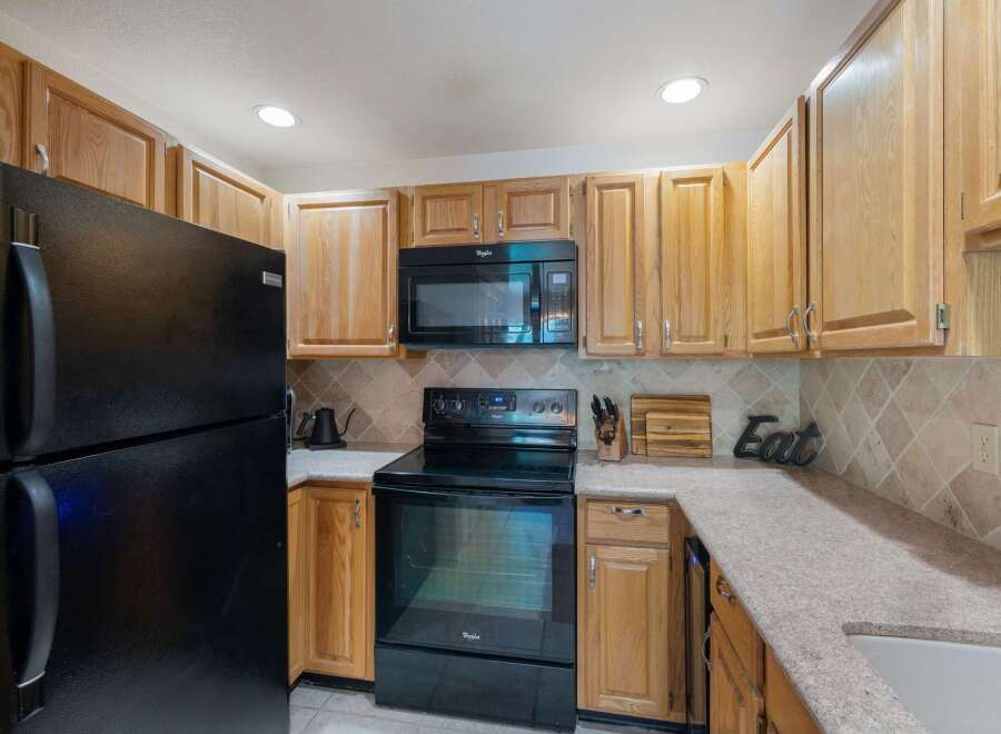 This charming kitchen features light wood cabinetry and a sleek black appliance suite, including a refrigerator, microwave, and oven.