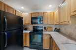 This charming kitchen features light wood cabinetry and a sleek black appliance suite, including a refrigerator, microwave, and oven.