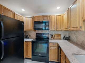This charming kitchen features light wood cabinetry and a sleek black appliance suite, including a refrigerator, microwave, and oven.