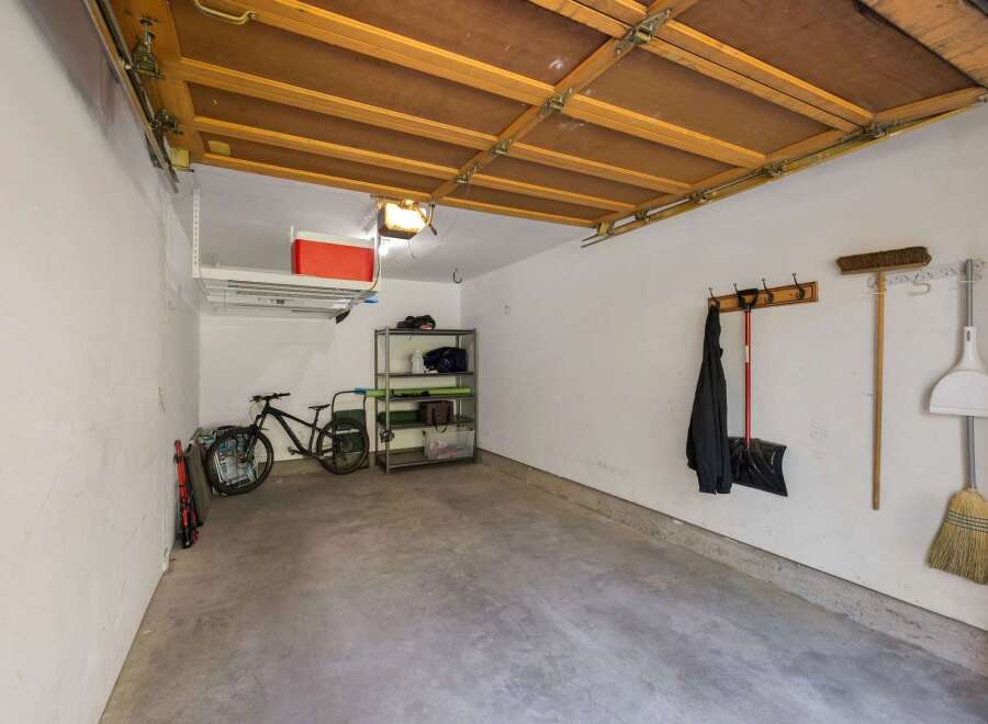 This spacious garage offers ample storage solutions, including overhead shelving and a multi-tiered rack, perfect for organizing tools and equipment.