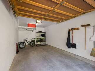 This spacious garage offers ample storage solutions, including overhead shelving and a multi-tiered rack, perfect for organizing tools and equipment.