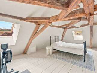 Experience rustic charm in this attic bedroom, featuring exposed wooden beams and a cozy sloped ceiling.
