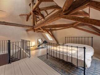 Discover this unique attic bedroom featuring exposed wooden beams and a charming spiral staircase.