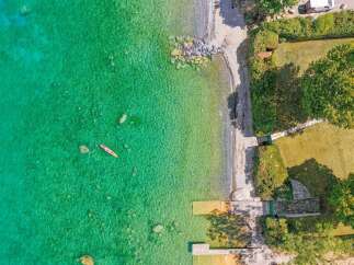 Experience serene lakeside living with this stunning aerial view of a property featuring crystal-clear turquoise waters perfect for kayaking.