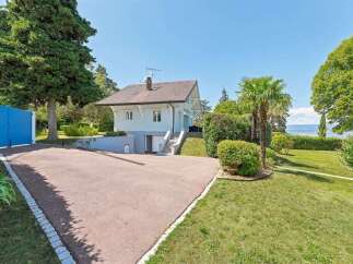 Discover this charming property featuring a light-colored house with a pitched roof, set amidst lush greenery and mature trees.
