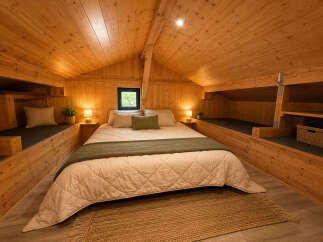 Experience cozy living in this charming wooden cabin bedroom, featuring a comfortable queen-size bed adorned with plush linens and a soft green throw.
