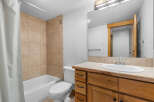 This bathroom features a tiled shower-tub combination with a white shower curtain, a white toilet, and a wooden vanity with a beige countertop and a white sink.