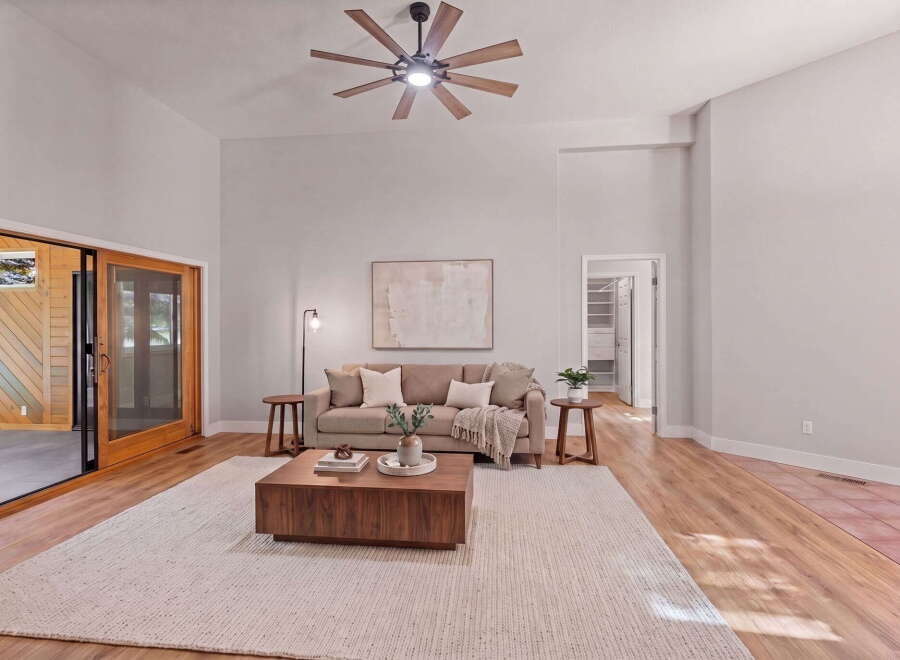 Experience modern living in this spacious living room featuring a vaulted ceiling with a stylish fan and a large sliding glass door that opens to a serene outdoor space.