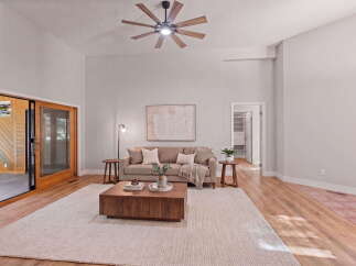 Experience modern living in this spacious living room featuring a vaulted ceiling with a stylish fan and a large sliding glass door that opens to a serene outdoor space.