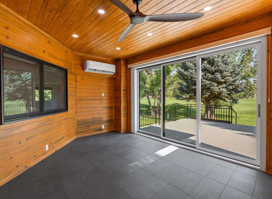 Enjoy the outdoors from this charming sunroom, featuring a modern ceiling fan and a convenient air conditioning unit for year-round comfort.