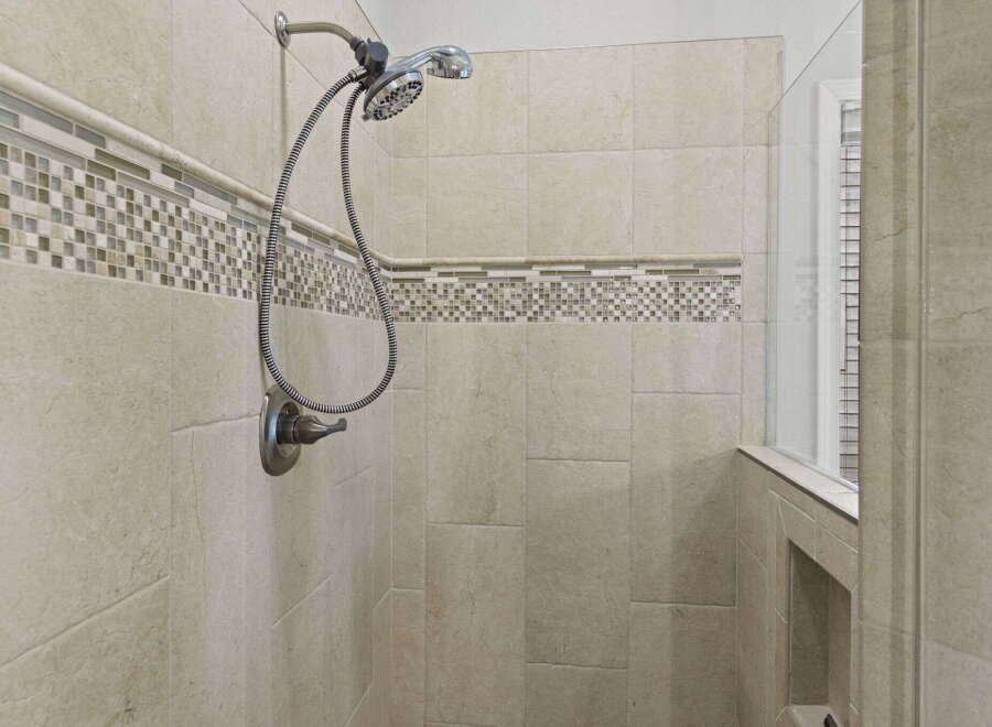 Experience luxury in this modern shower featuring elegant beige tiled walls accented with a decorative mosaic tile border.