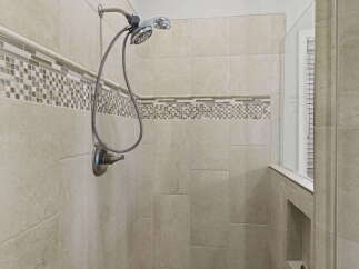 Experience luxury in this modern shower featuring elegant beige tiled walls accented with a decorative mosaic tile border.