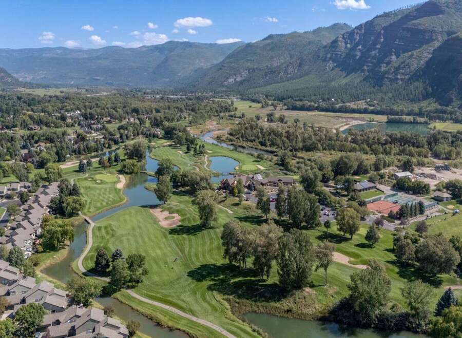 Experience luxury living with this stunning aerial view of a golf course community nestled beside a serene river and majestic mountains.
