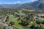 Experience luxury living with this stunning aerial view of a golf course community nestled beside a serene river and majestic mountains.