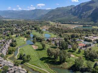 Experience luxury living with this stunning aerial view of a golf course community nestled beside a serene river and majestic mountains.