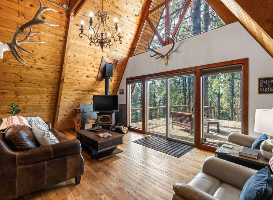 Experience rustic charm in this A-frame cabin living room, featuring a stunning antler chandelier and a cozy fireplace.