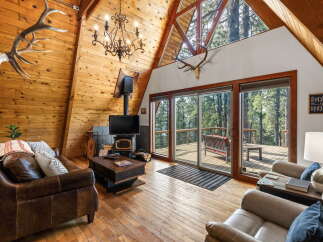 Experience rustic charm in this A-frame cabin living room, featuring a stunning antler chandelier and a cozy fireplace.